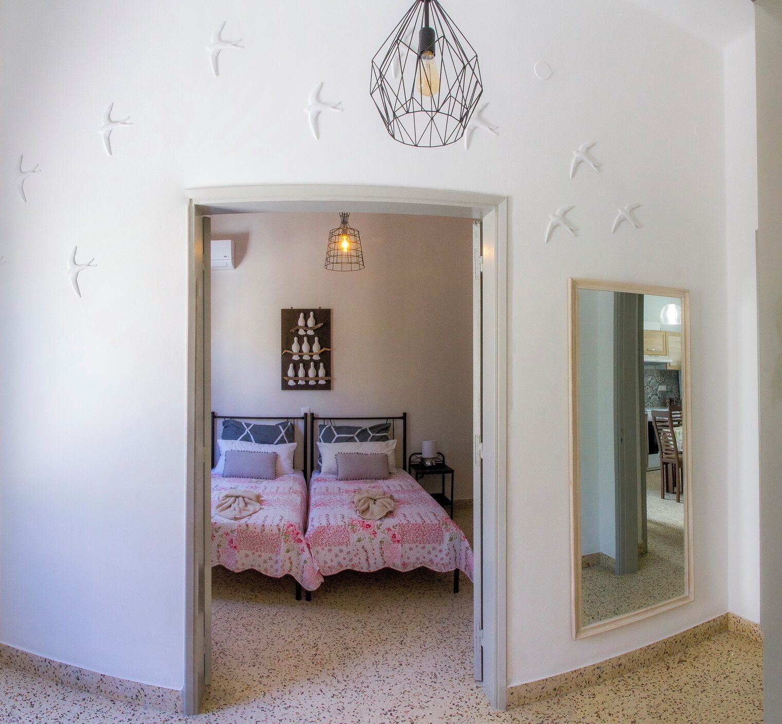 A bedroom with two beds, a hanging light fixture, a wall-mounted decoration, and a mirror.