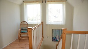 A staircase with wooden railings leading to a landing with two windows, a wicker chair with a cushion, and a painting on the wall. - Casa Azul Seaside House 10 minutes from Gdynia, 25 minutes from Gdańsk. 15 min. Sopot (Kosakowo)