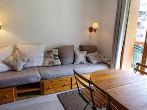 Quarto aconchegante com sofá, mesa de madeira e luminária na parede.