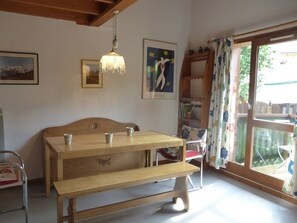 Quarto com um banco de madeira, uma mesa, luminária pendente e janela com cortinas.