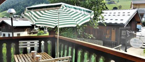 Un balcon avec une table et un banc en bois, un parasol à rayures et une vue sur un paysage montagneux.