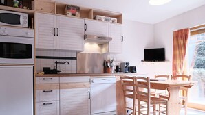 A compact kitchen with white cabinetry, a dining table with chairs, a television, and a window with curtains. - Cosy Apt with Pool Access, Near Slopes & Shops, Sleeps 3 (Arêches-Beaufort)