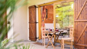 A wooden barn-style room with a table and chairs, a window with curtains, and a view of greenery outside. - Cosy Apt with Pool Access, Near Slopes & Shops, Sleeps 3 (Arêches-Beaufort)