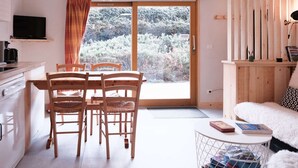 A cozy room with a dining table, chairs, a sofa, a TV, and a large window with a view of trees. - Cosy Apt with Pool Access, Near Slopes & Shops, Sleeps 3 (Arêches-Beaufort)