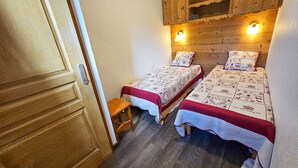 Une petite chambre agréable, dotée de deux lits simples, de placards en bois au-dessus et d’un petit tabouret.