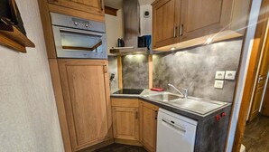 Une cuisine compacte avec des meubles en bois, un four encastré, un lave-vaisselle et un plan de travail en granit.