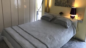 A neatly made bed with a striped bedspread and pillows, a bedside lamp, and a wall art piece above the bed.