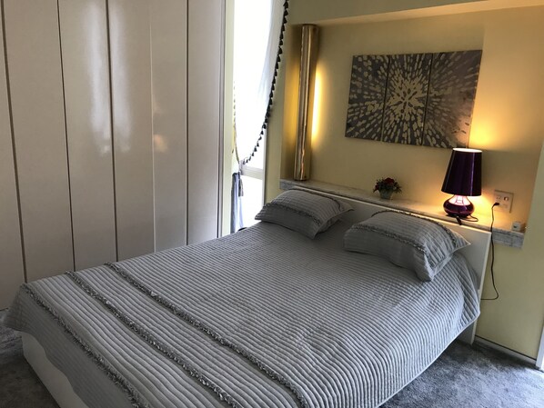 Un lit bien fait, avec une couvre-lit à rayures et des oreillers, une lampe de chevet et une œuvre d’art accrochée au mur au-dessus du lit.