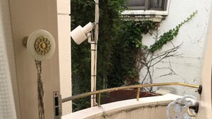 A small balcony with a white chair, a metal railing, and a door with a rope decoration.