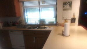 A kitchen with wooden cabinets, a dishwasher, a sink, and a window with blinds. - Spacious Corner House  NO POOL HOWEVER BEAUTIFUL  PROFESSIONAL POOL TABLE (Cape Coral)
