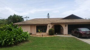 A single-story house with a sloped roof, a garage, and a well-maintained lawn. - Spacious Corner House  NO POOL HOWEVER BEAUTIFUL  PROFESSIONAL POOL TABLE (Cape Coral)
