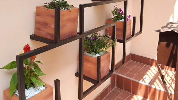 Een houten plantenplank met verschillende potplanten tegen een muur.