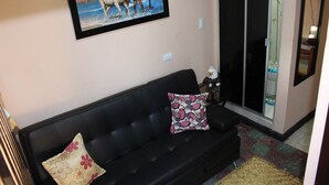 Een woonkamer met een zwarte bank, twee gestreepte kussens, een gekaderd schilderij van paarden en een deur met een bamboepatroon.