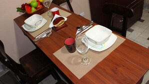 Een eettafel gedekt met borden, bestek, een glas, een fruitschaal en een koffiemok.