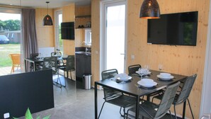 A modern dining area with a black table set for four, surrounded by black chairs. A kitchen area is visible in the background with a sink and cabinets. - Holiday home Callants` Lodge (Callantsoog)