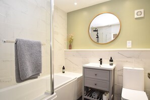 A bathroom with a bathtub, a toilet, a sink with a mirror, and a towel rack. - Daisy Cottage, Sleeps 2 - Romantic Retreat in Rye, East Sussex, UK (Rye)