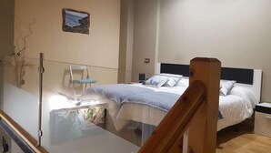A bedroom with a bed, a chair, and a small table. There is a picture on the wall and a window with a view of the outside.