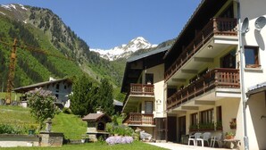 A hotel with multiple balconies, a garden area with flowers, and a mountainous backdrop. - Cozy 30m² Apt for 4 at Planay Slopes avec Balcony, Parking & Heated Ski Room (Arêches-Beaufort)