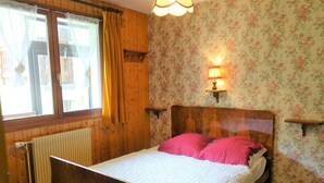 A bedroom with a wooden bed, floral wallpaper, a radiator, and a window with curtains. - Cozy 30m² Apt for 4 at Planay Slopes avec Balcony, Parking & Heated Ski Room (Arêches-Beaufort)