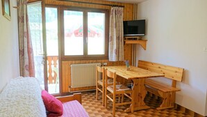 A room with a bed, a wooden table with chairs, a TV on a shelf, and a window with curtains. - Cozy 30m² Apt for 4 at Planay Slopes avec Balcony, Parking & Heated Ski Room (Arêches-Beaufort)