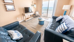 A living room with a sofa, a television, a chair, and a view of the ocean through a sliding door. - Oceanfront Corner Unit 2BR Condo 5th Floor Balcony Views, 501 (Indian Harbour Beach)