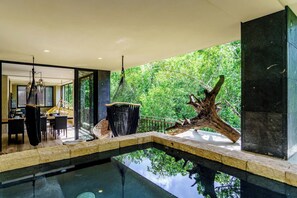 A modern interior with a pool, a dining area, and a view of lush greenery. - Aldea Zama Condo: Private Pool, Gym & Spa (Tulum)