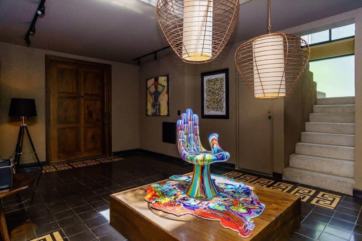 Un hall d’entrée avec un plancher en bois, une porte en bois, un escalier et une sculpture abstraite aux couleurs vives, placée sur une plateforme en bois.