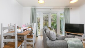 A living room with a sofa, TV, dining table, chairs, and a view through a glass door. - Honeysuckle Cottage, Lelant – Sleeps - On-Site Parking – Dog Friendly (Lelant)