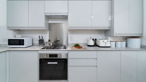 A modern kitchen with white cabinetry, a microwave, a stove, an oven, and a coffee maker. - Honeysuckle Cottage, Lelant – Sleeps - On-Site Parking – Dog Friendly (Lelant)