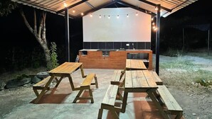 Een openluchttheater met een groot scherm, houten banken en een overdekt zitgedeelte.