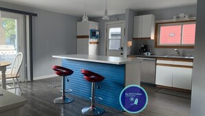 A modern kitchen with a blue accent wall, white cabinets, and two red bar stools. - Big DECK Cottage, 3-min walk to BEACH- 4 bdrms, 1.5 baths 7 beds, parking 3 cars (Grand Bend)
