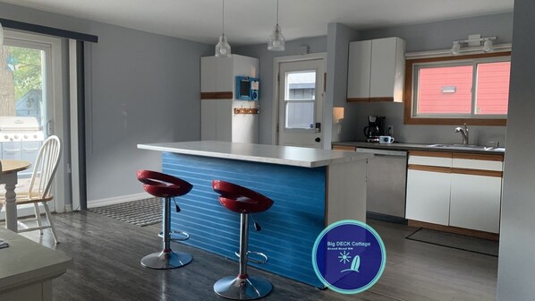 A modern kitchen with a blue accent wall, white cabinets, and two red bar stools.
