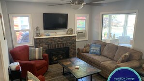 A living room with a fireplace, a television, and a ceiling fan. There are two sofas and a coffee table. - Big DECK Cottage, 3-min walk to BEACH- 4 bdrms, 1.5 baths 7 beds, parking 3 cars (Grand Bend)