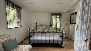 A bedroom with a bed, a sofa, a lamp, and a window with blinds.