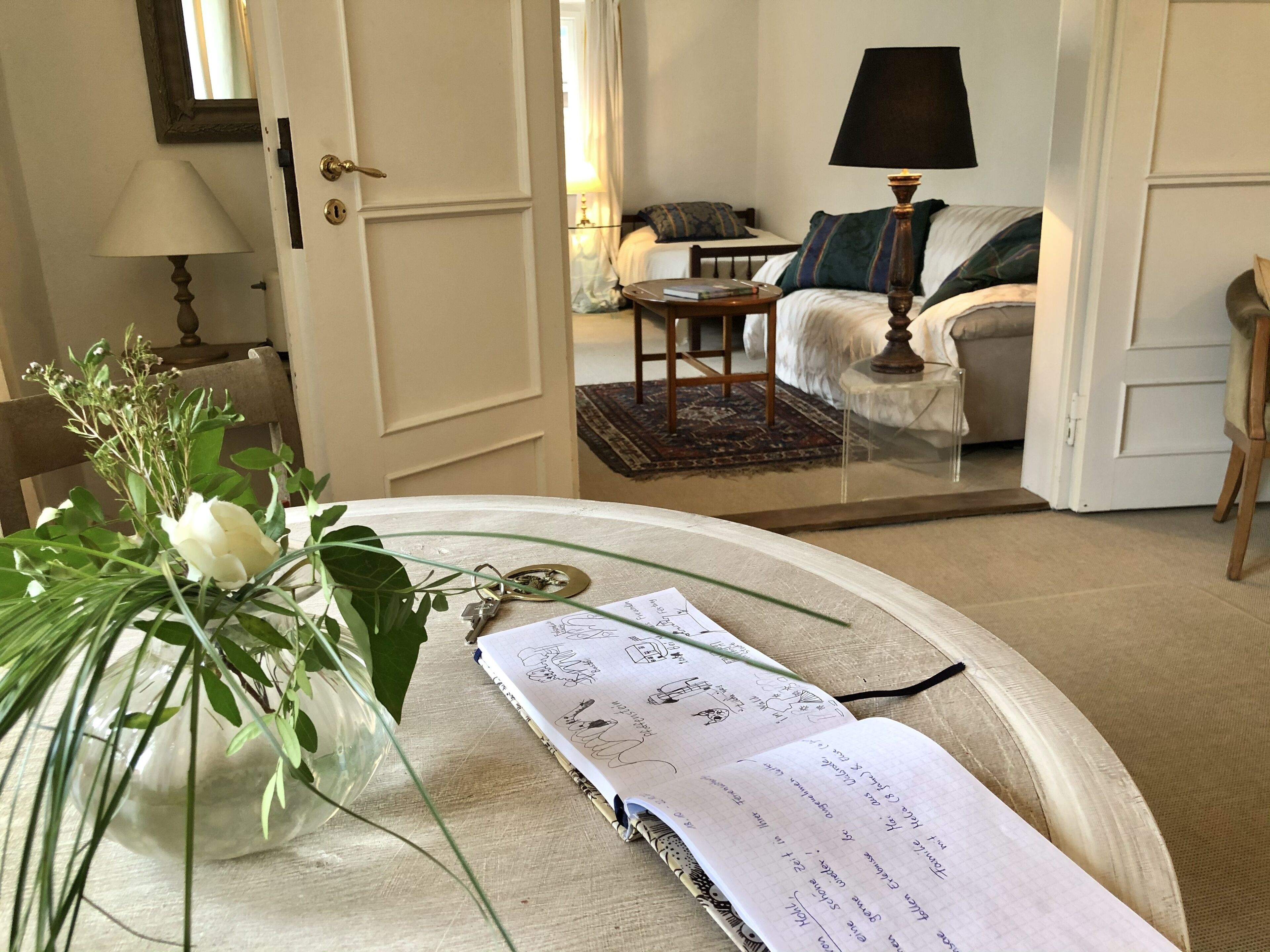 Ein Zimmer mit einem Bett, einem Sessel, einem Tisch mit Blumen und einem Buch.