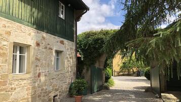 Ein Kopfsteinpflasterhof mit Steinmauern, einem grünen Holzgebäude und einem Blumentopf.