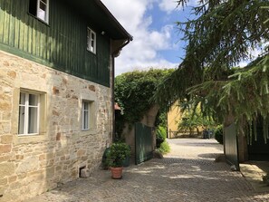 Ein Kopfsteinpflasterhof mit Steinmauern, einem grünen Holzgebäude und einem Blumentopf.