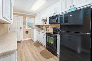 Kitchen features a refrigerator, oven, and microwave, with a light wood floor and window with blinds.