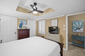 Un dormitorio con una cama, ventilador de techo, cómoda, televisor y obras de arte en las paredes.