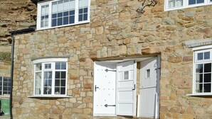 A stone building with two white-framed windows and a white door. - A delightful fisherman’s cottage with uninterrupted sea views. (Staithes near Whitby)