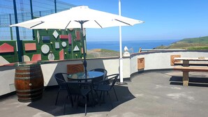 An outdoor patio with a round table and chairs, a wooden barrel, and a white umbrella. - Apartment Santa Justa (Santillana del Mar)