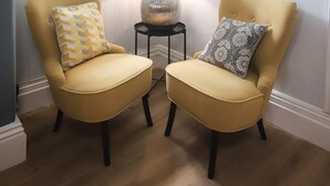 A room with two yellow armchairs, a small side table with a lamp, and three framed pictures on the wall.