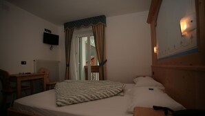 A bedroom with a bed, a desk, a chair, a television, and a mirror. - Garnì Eden (Canazei)