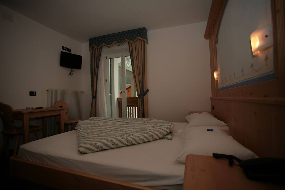 A bedroom with a bed, a desk, a chair, a television, and a mirror.