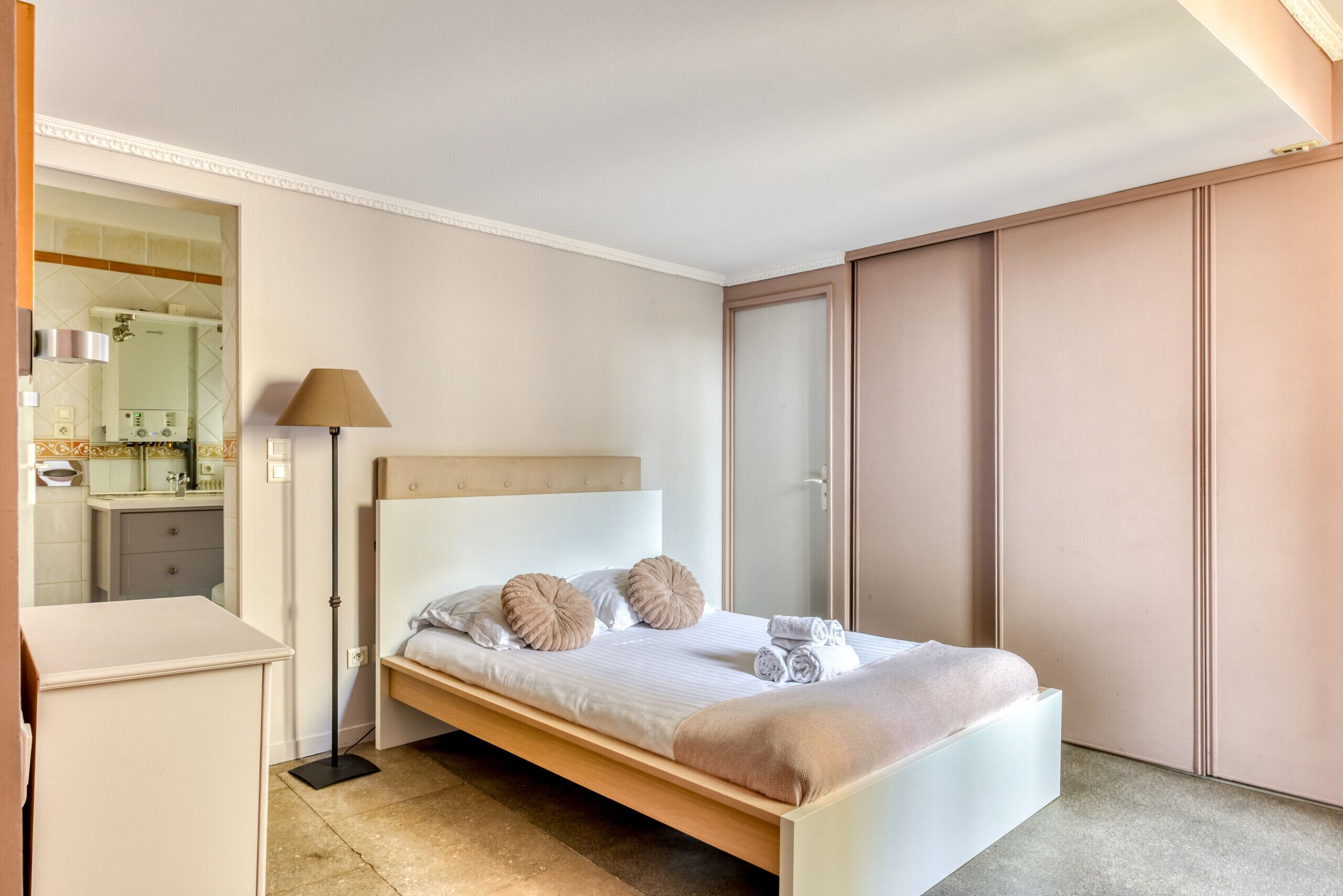 A bedroom with a bed, a bedside table, a lamp, and a wardrobe.