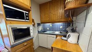 Une cuisine compacte dotée de meubles en bois, d’un four à micro-ondes, d’un four, d’un évier et d’une bouilloire.