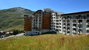 Un hôtel moderne à plusieurs étages, dont la façade est composée d’un mélange de panneaux en bois et de panneaux blancs, situé dans une région montagneuse sous un ciel dégagé.