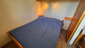 Une petite chambre avec un lit simple, une tête de lit en bois, une table de chevet et un placard au-dessus du lit.
