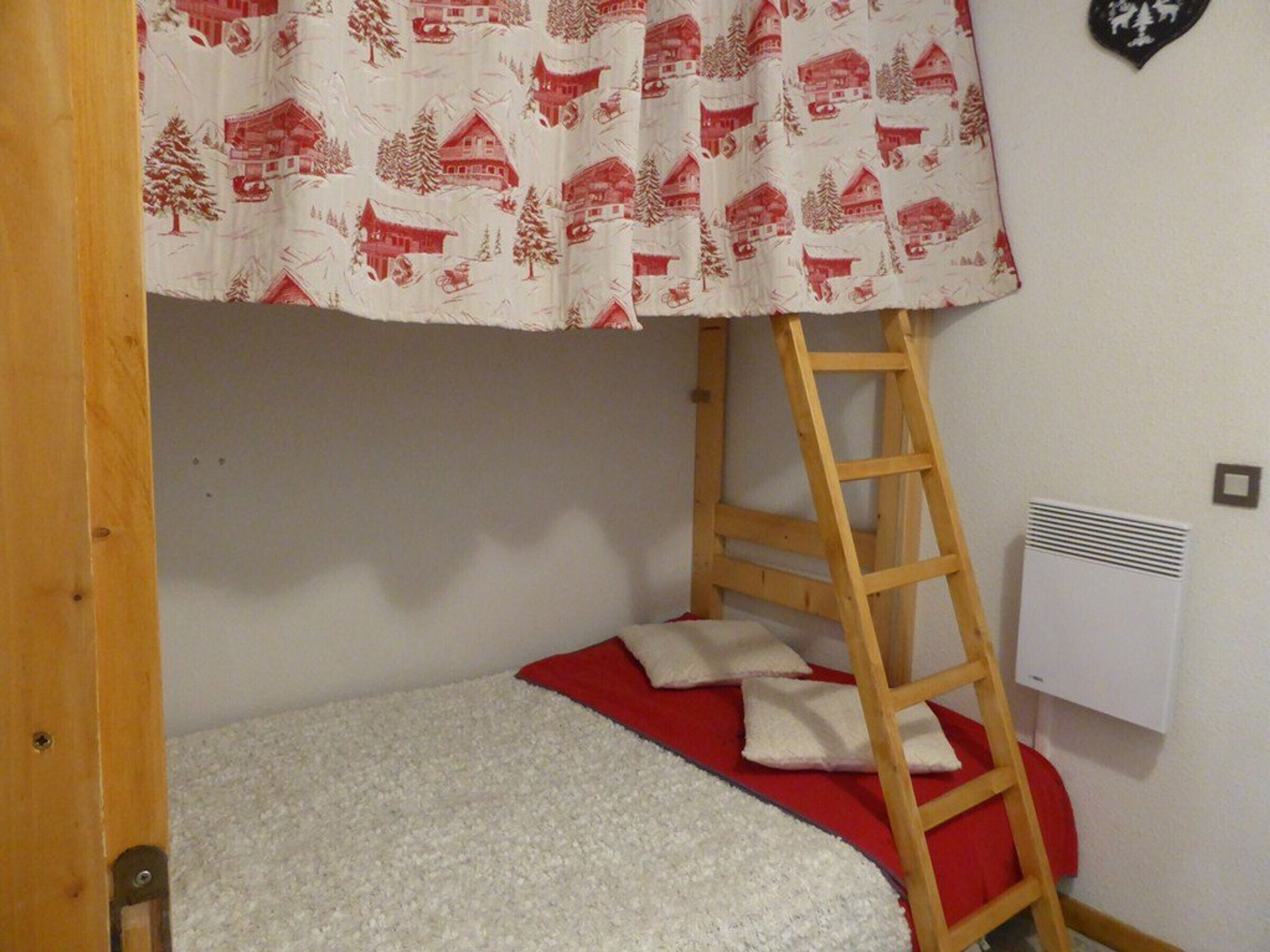 A bunk bed with a red and white patterned canopy, a wooden ladder, and a white mattress.