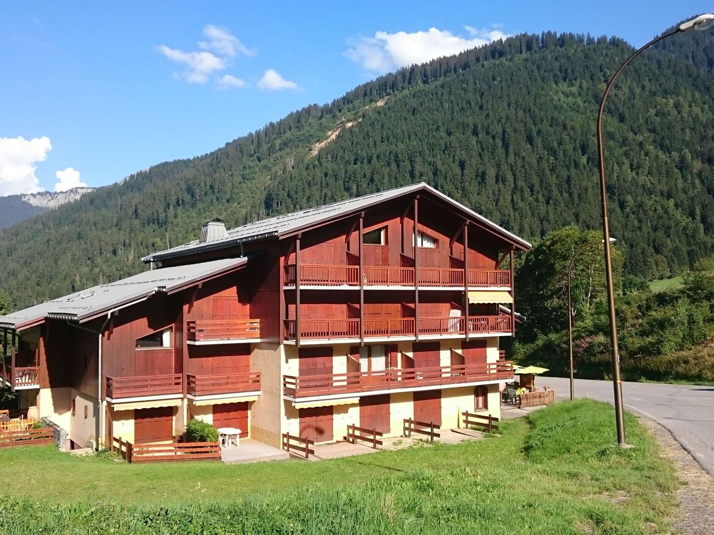 A two-story wooden building with balconies, a sloped roof, and a view of a forested mountain.